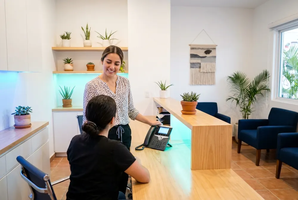 Recepción de una clínica con el teléfono sonando mientras la recepcionista atiende a una paciente